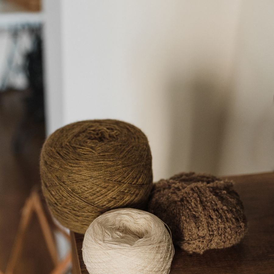 Three balls of wool in oatmeal and olive on a wooden table